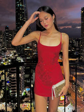 Woman in a red dress standing on a balcony with a cityscape background at night.